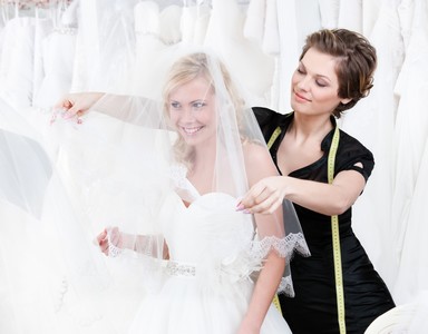 Shop assistant sets the veil of the bride, white background